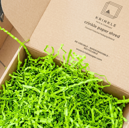 Box filled with green crinkle paper shred, branded as Krinkle Paper & Company.